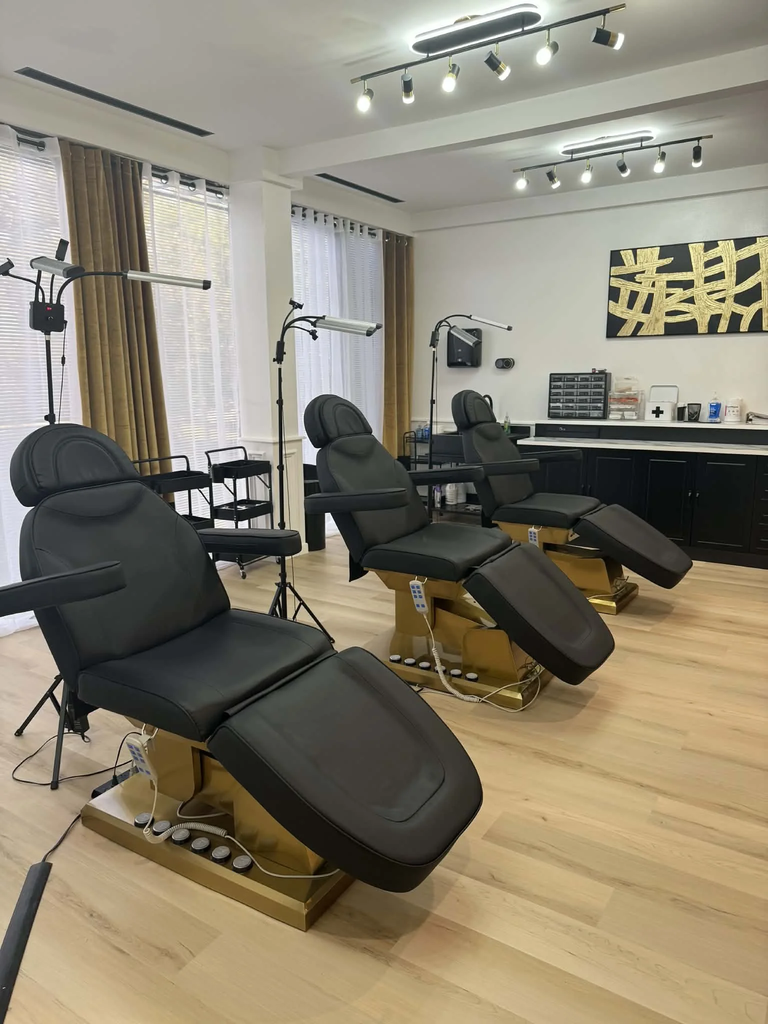 Three black and gold adjustable chairs in a well-lit modern medical or beauty treatment room.