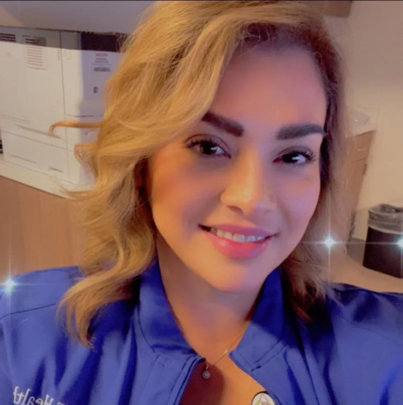 Smiling woman with blonde hair wearing a blue jacket in an office setting.