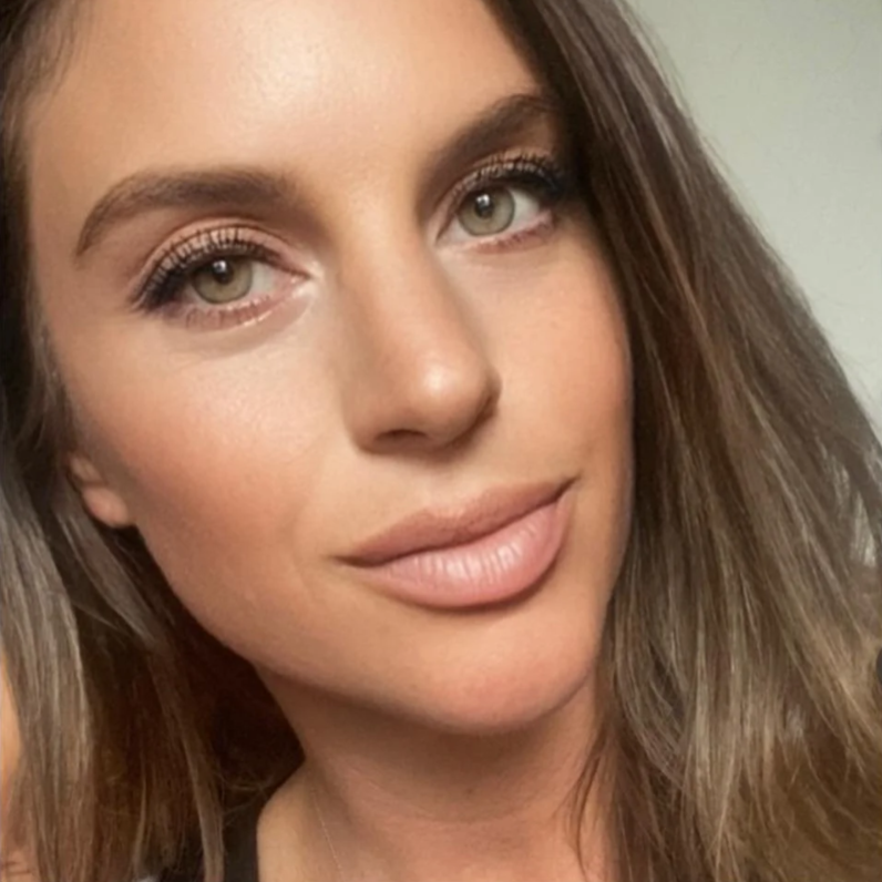 Close-up portrait of a woman with light makeup and long brown hair against a neutral background.