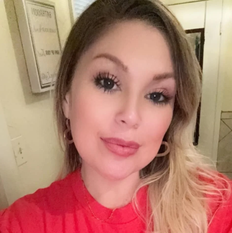 Close-up portrait of a woman with long blonde hair wearing a red top and hoop earrings indoors.
