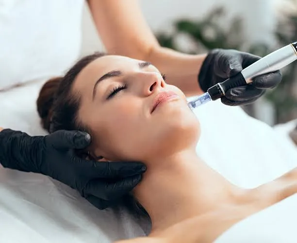 Woman receiving a facial skin treatment with a handheld device by a professional wearing black gloves.