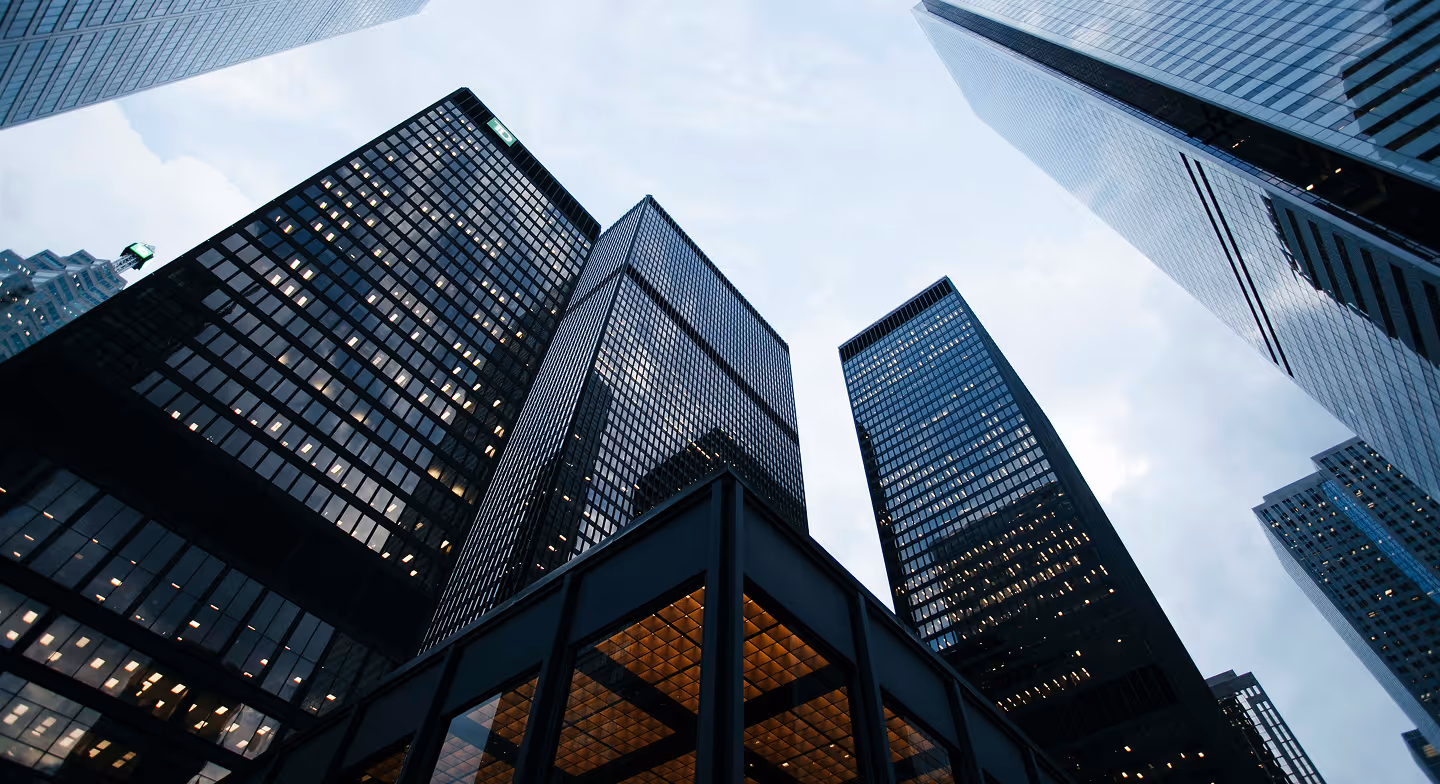 Low-angle view of tall modern skyscrapers with lit windows under a cloudy sky.