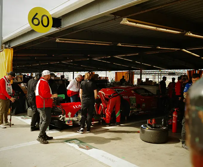 Race team works on a red race car in a garage with a yellow 60 sign overhead.