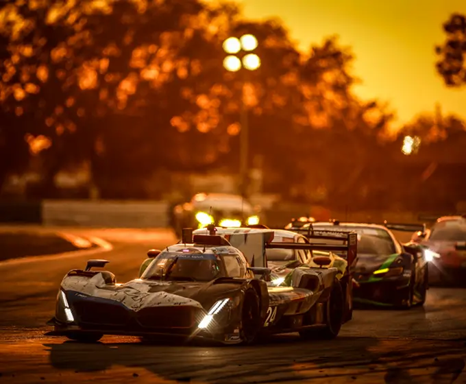 Race cars on track during sunset under warm golden light and blurred trees in background.