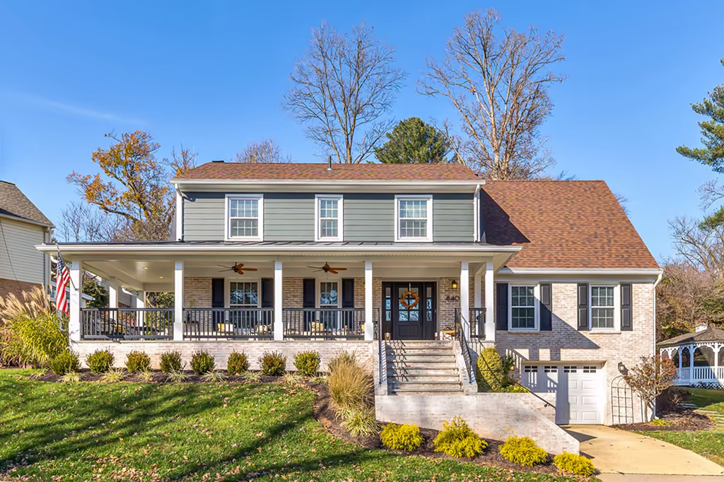 Two-story home with a wide covered porch, gray siding, brick exterior, black shutters, and an attached garage.