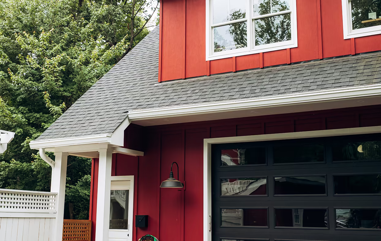 Red board-and-batten garage exterior with a black modern garage door, gray shingle roof, and white trim.