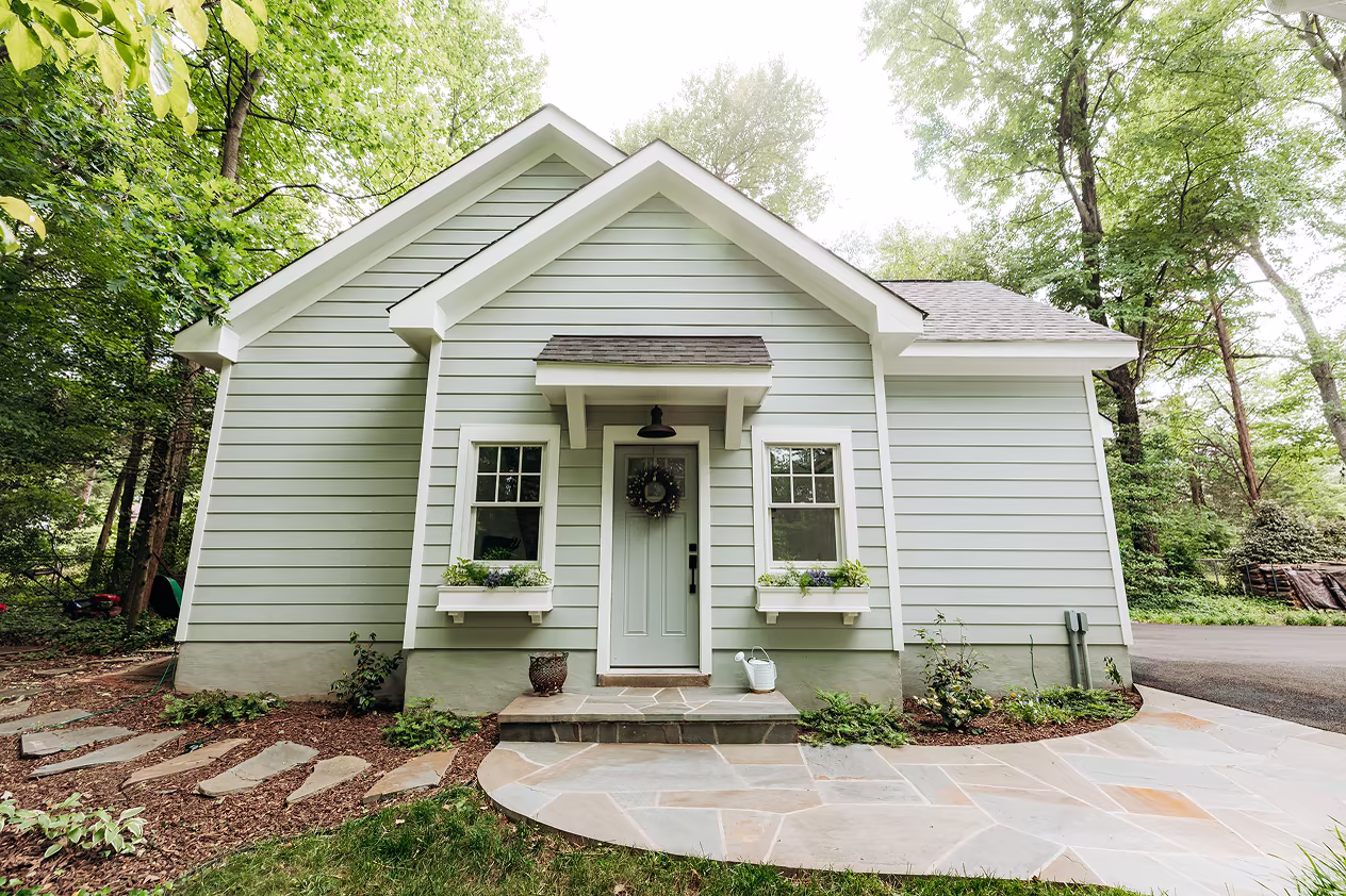 Light green cottage-style home with white trim, front gables, window boxes, and a curved stone entry patio.