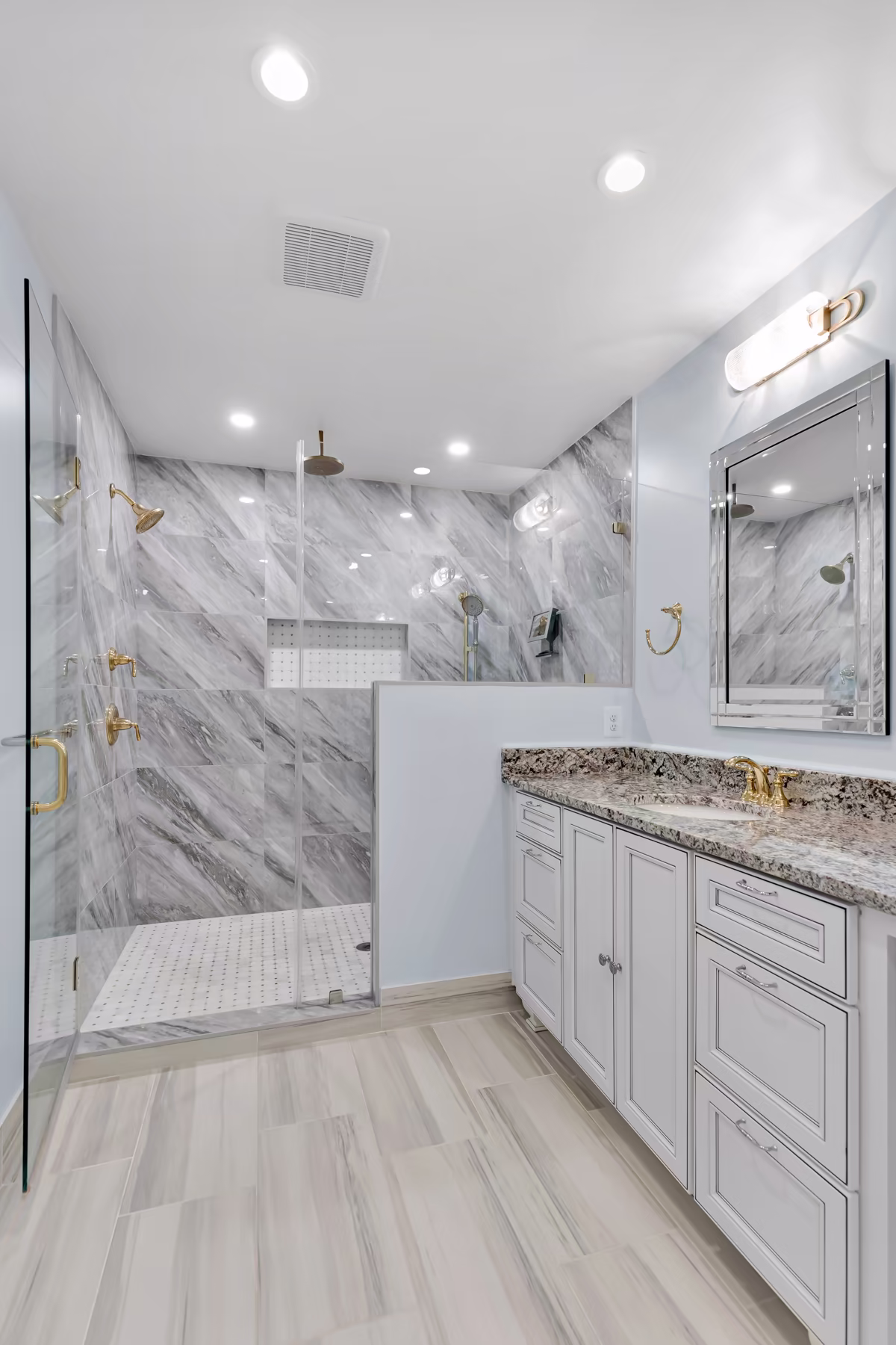  Luxury bathroom featuring a large walk-in marble shower with brass fixtures, white vanity with granite countertop, and light wood-look tile floor.