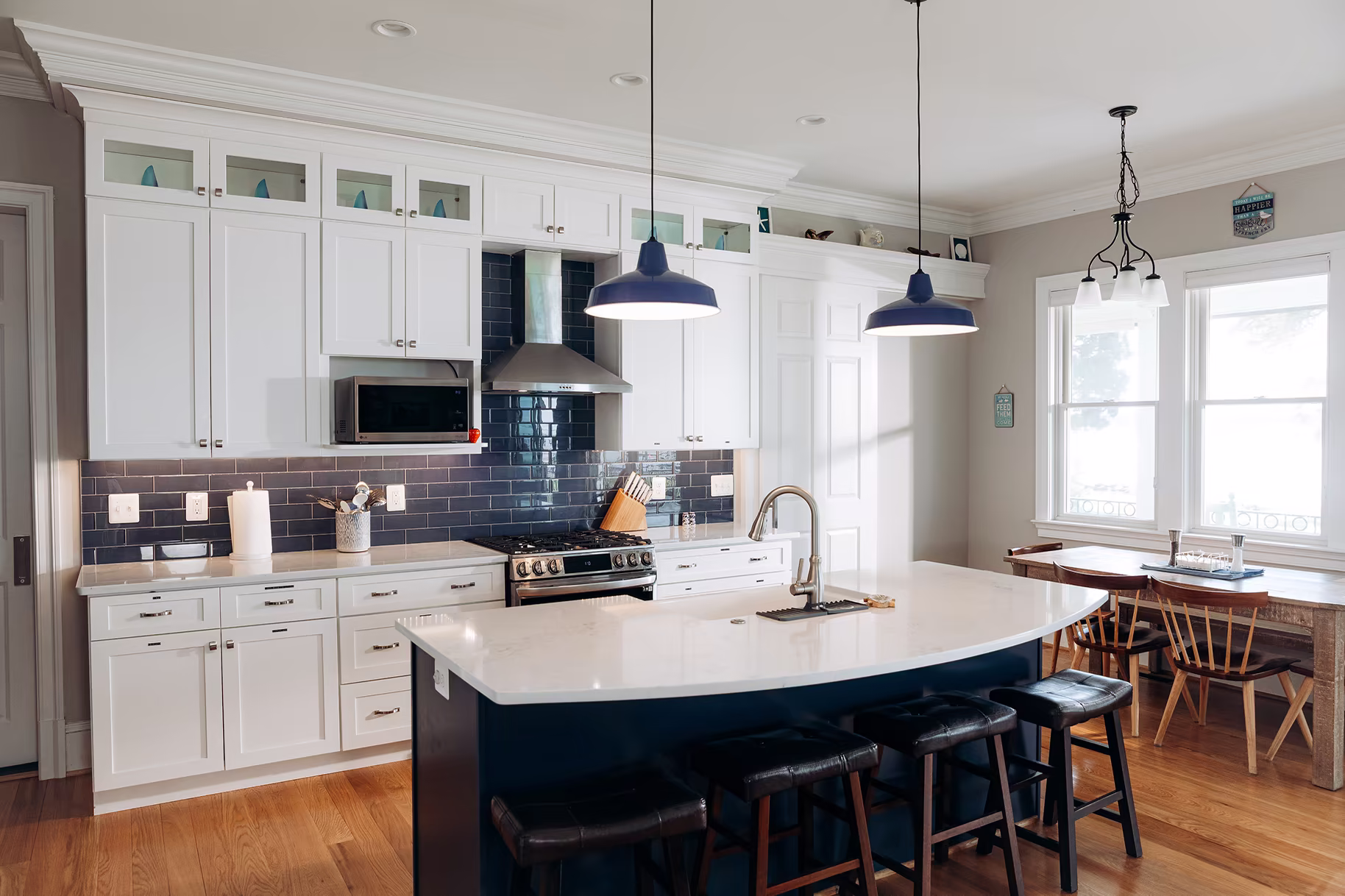 Bright white kitchen with navy subway-tile backsplash, blue pendant lights, and a large dark-blue island with seating.
