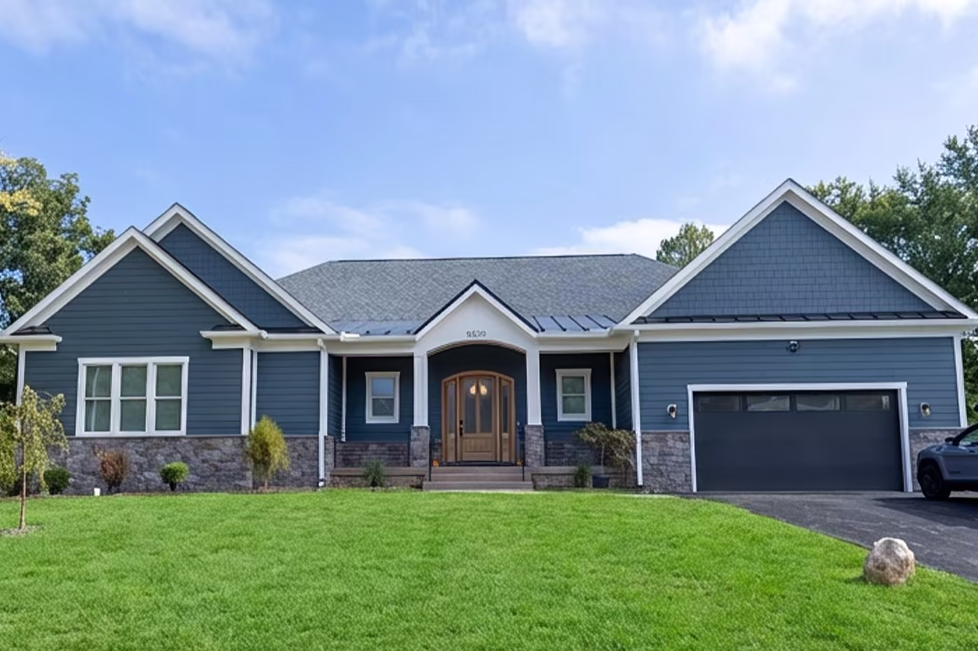 Gray shingle-style two-story home with a wraparound porch, white trim, and a picnic table on the lawn at sunset