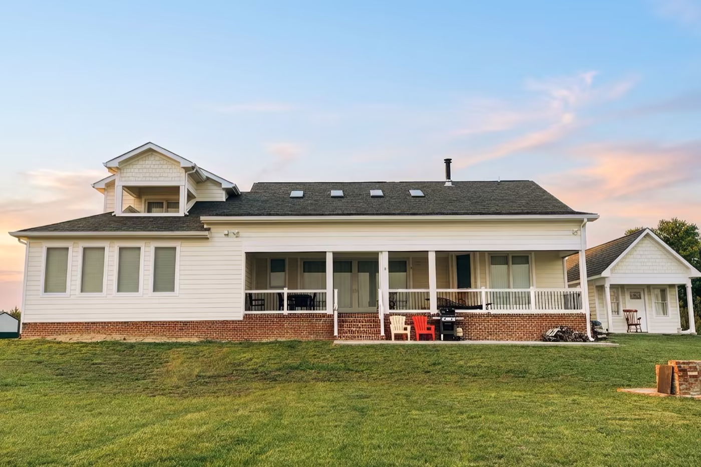White farmhouse with a covered front porch, skylights, and a red Adirondack chair, lit at sunset