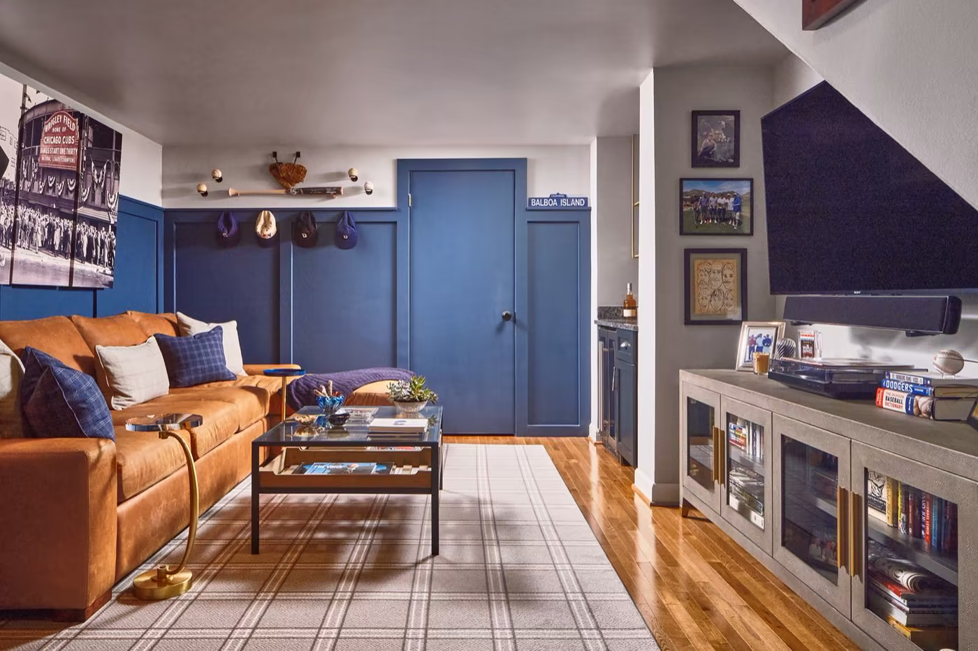 Basement rec room with navy blue paneled walls, a tan leather sofa, wall-mounted TV, and a sports memorabilia display