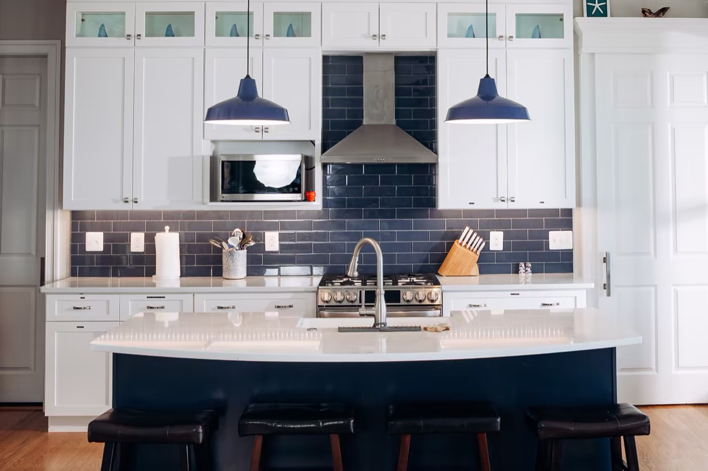 Kitchen with white cabinetry, navy blue subway tile backsplash, navy pendant lights, and black leather counter stools