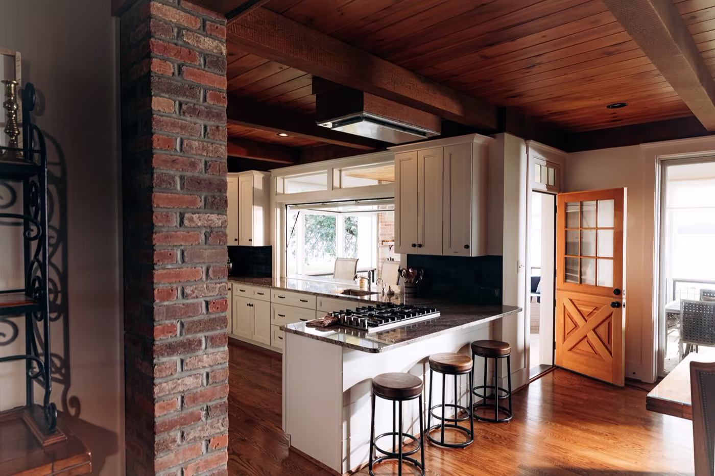 Kitchen with an exposed brick column, wood beam ceiling, cream cabinetry, and an orange X-paneled Dutch door