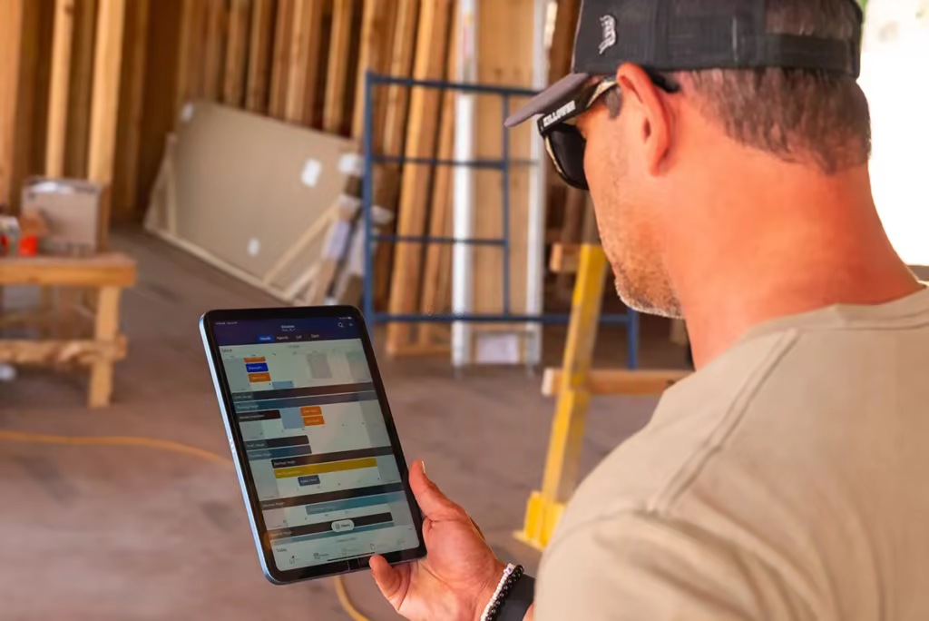 Contractor on a job site reviewing a construction schedule on a tablet using project management software.