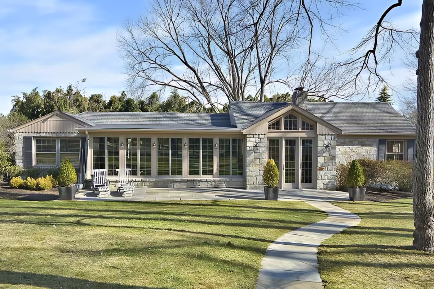 Ranch-style stone and shingle home with a glass-walled sunroom, covered entry, and a curved front walkway