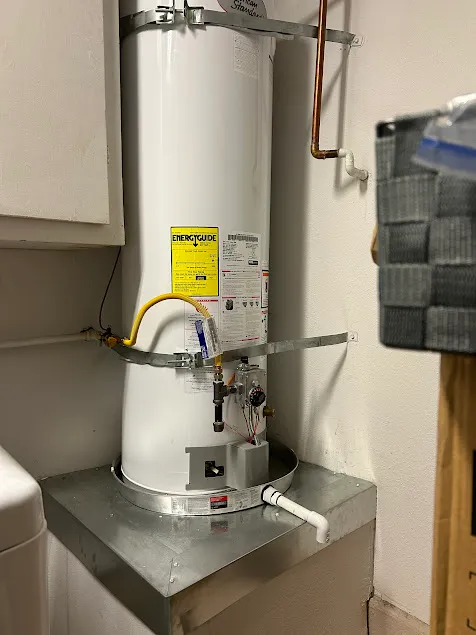Close-up of a premium natural gas water heater setup on a sheet metal base, highlighting a flawless gas valve and code-compliant sediment trap assembly