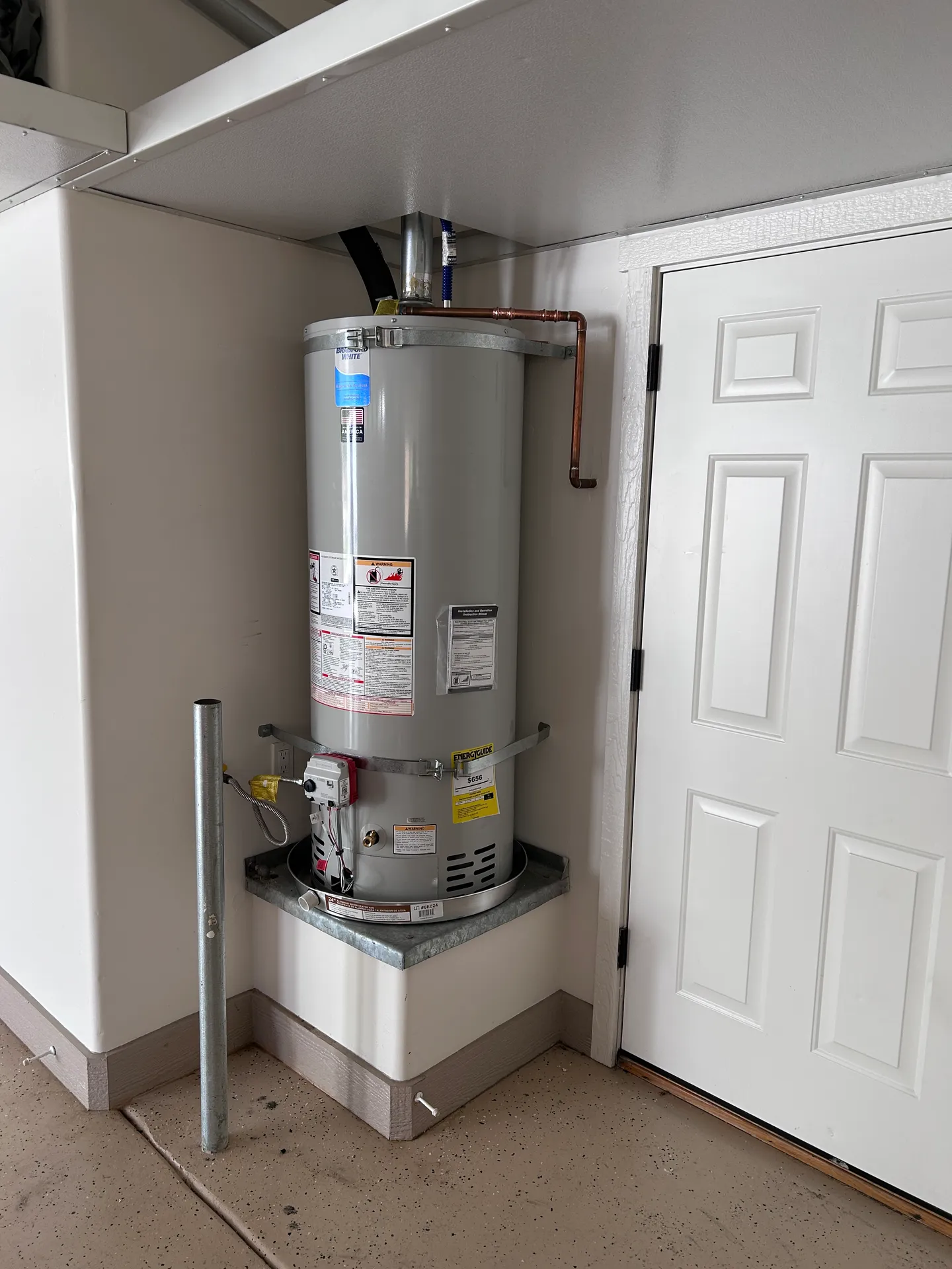 Precision 50-gallon gas water heater installation mounted on a custom-finished sheet metal base platform with code-compliant safety strapping.