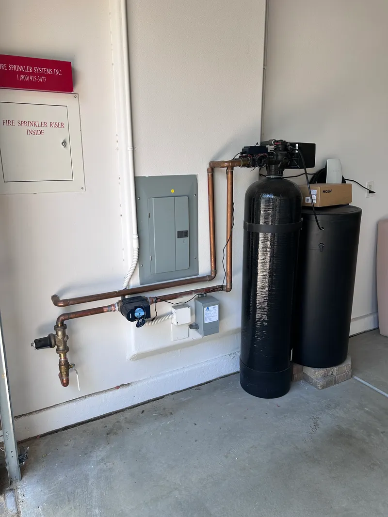 Close-up of a premium natural gas water heater setup on a sheet metal base, highlighting a flawless gas valve and code-compliant sediment trap assembly.