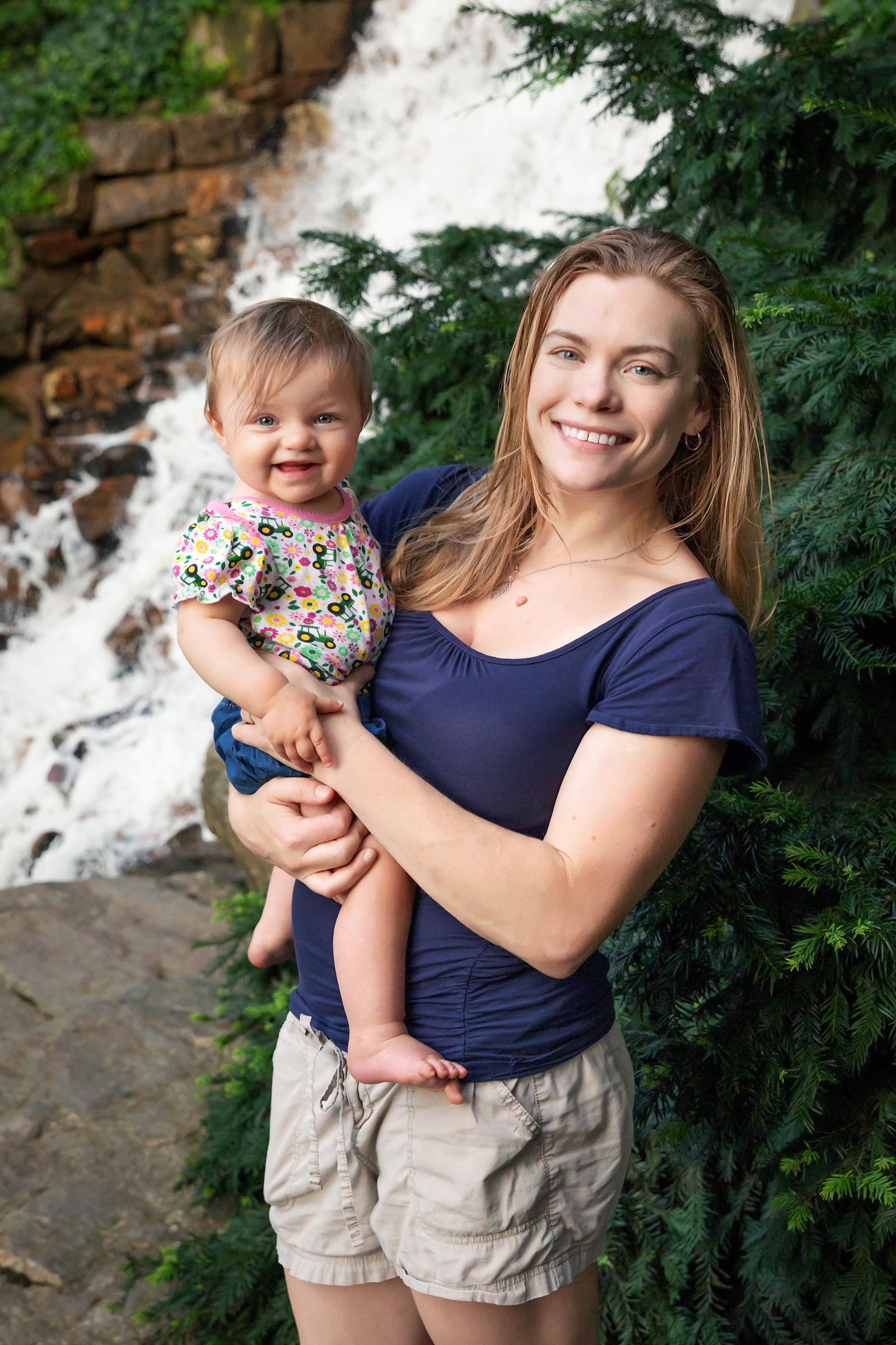 Portrait of Laura holding youngest daughter in front of waterfall.