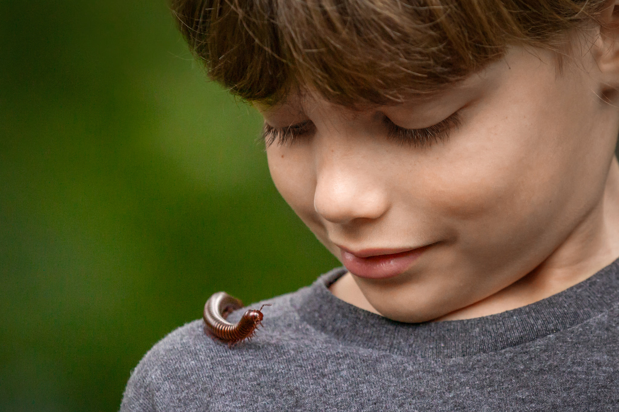 Close up portrait of young boy with his pet millipede on his shoulder, looking up at him