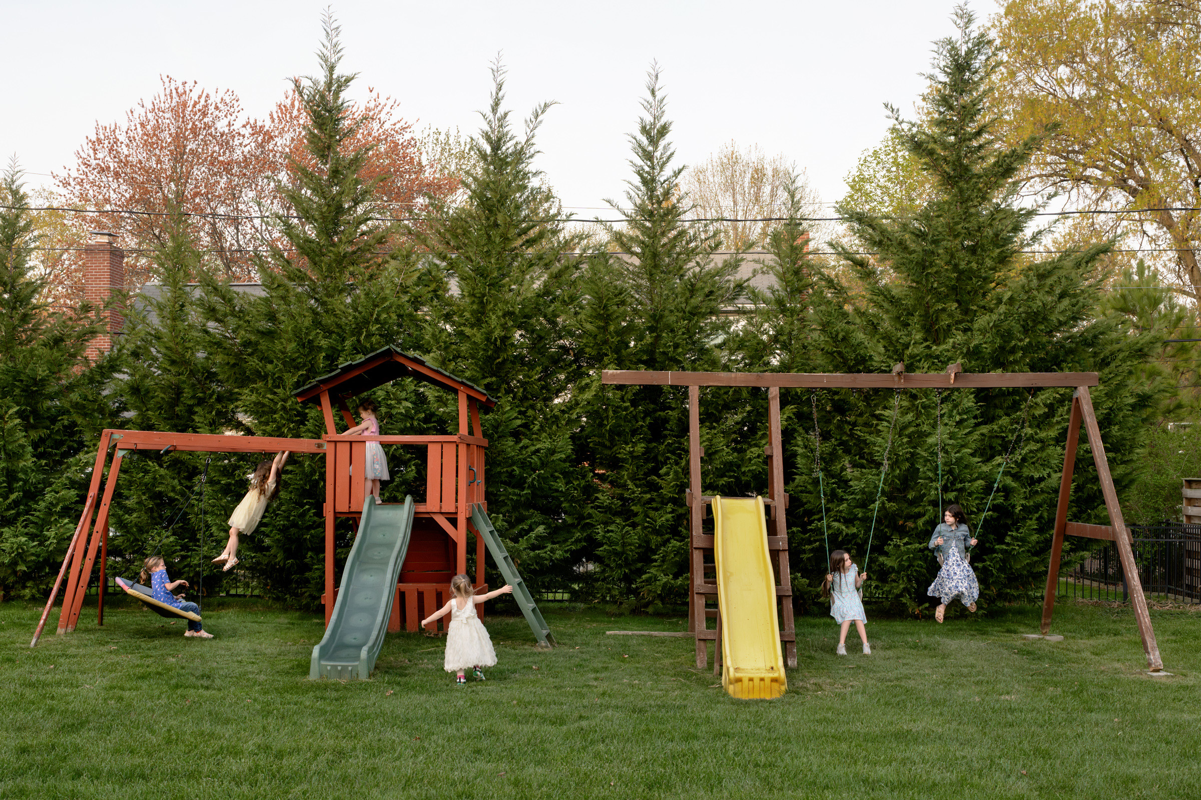 Five cousins play together on swings, slides, and a backyard playset during a family gathering.