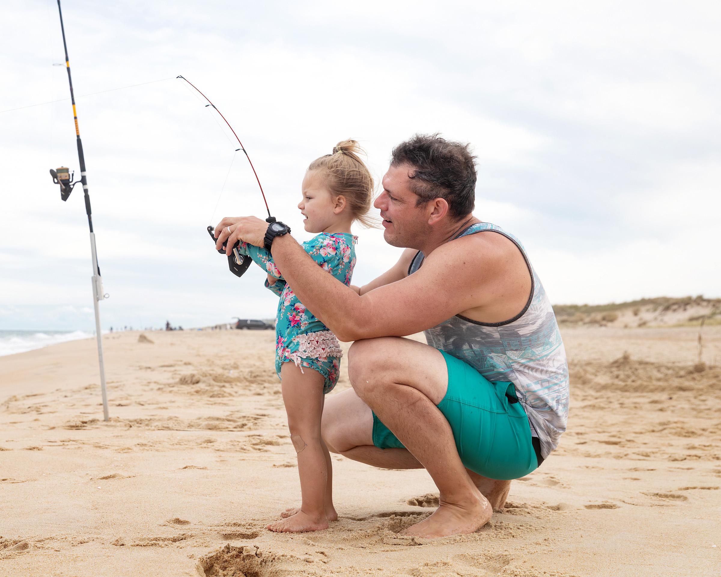 Father helping his young daughter fish from the beach.