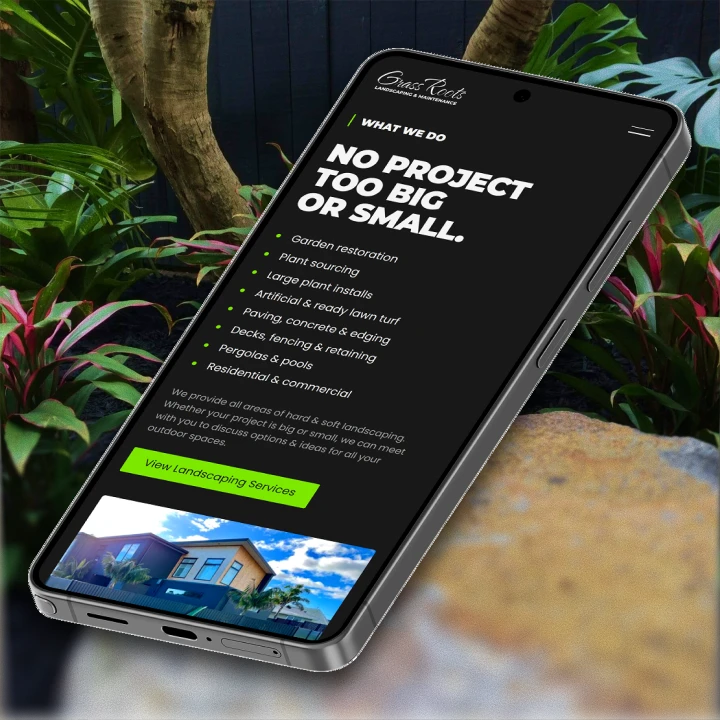 Smartphone displaying Grass Roots landscaping services webpage against garden background.