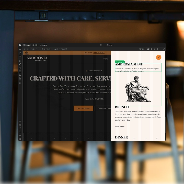 Computer screen showing Ambrosia restaurant website with menu overlay and text about crafted dishes.