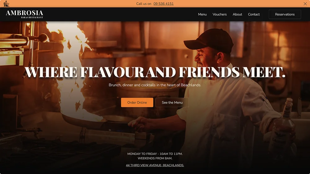 Chef in white uniform cooking with flames in a busy kitchen at Ambrosia Bar & Restaurant.