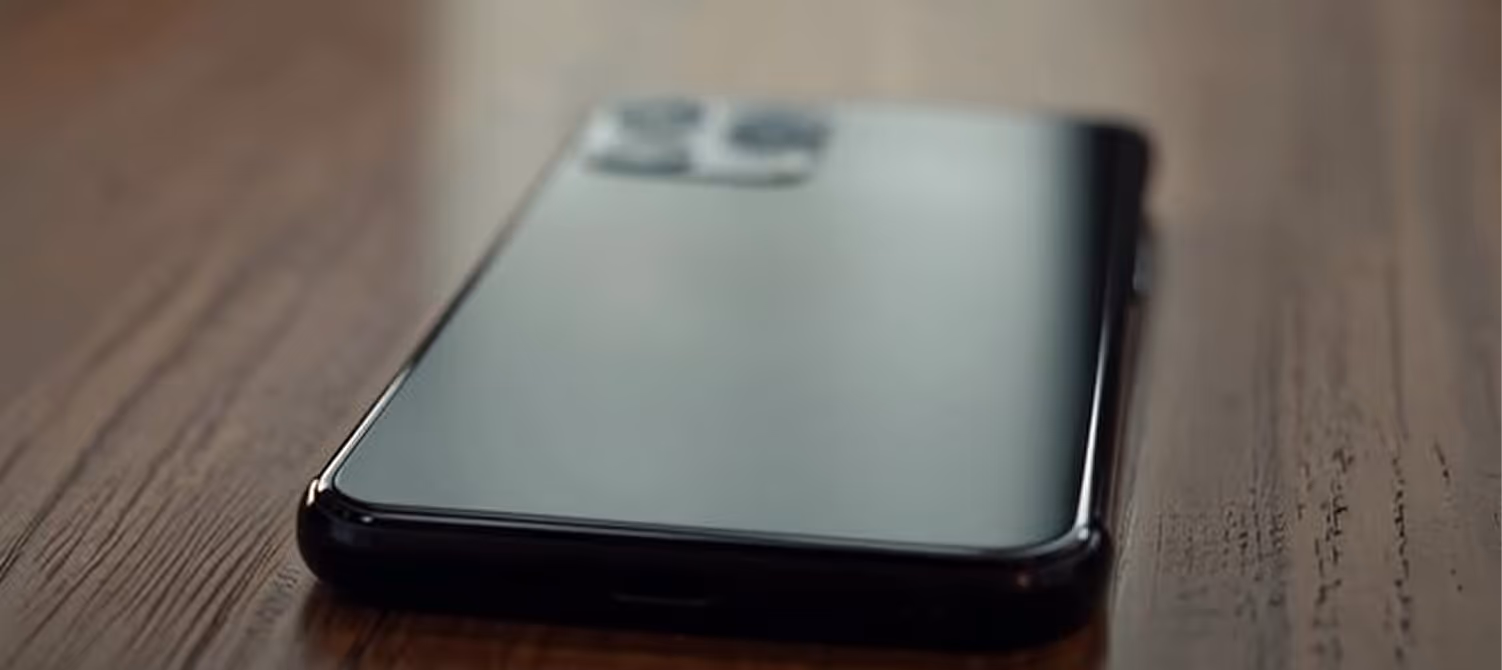 Black smartphone lying face down on wooden surface with rear cameras visible.