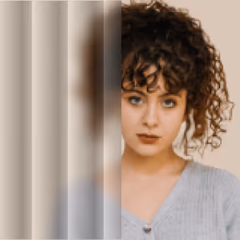 Woman with curly hair and blue eyes looking through a glass pane that blurs half her face.