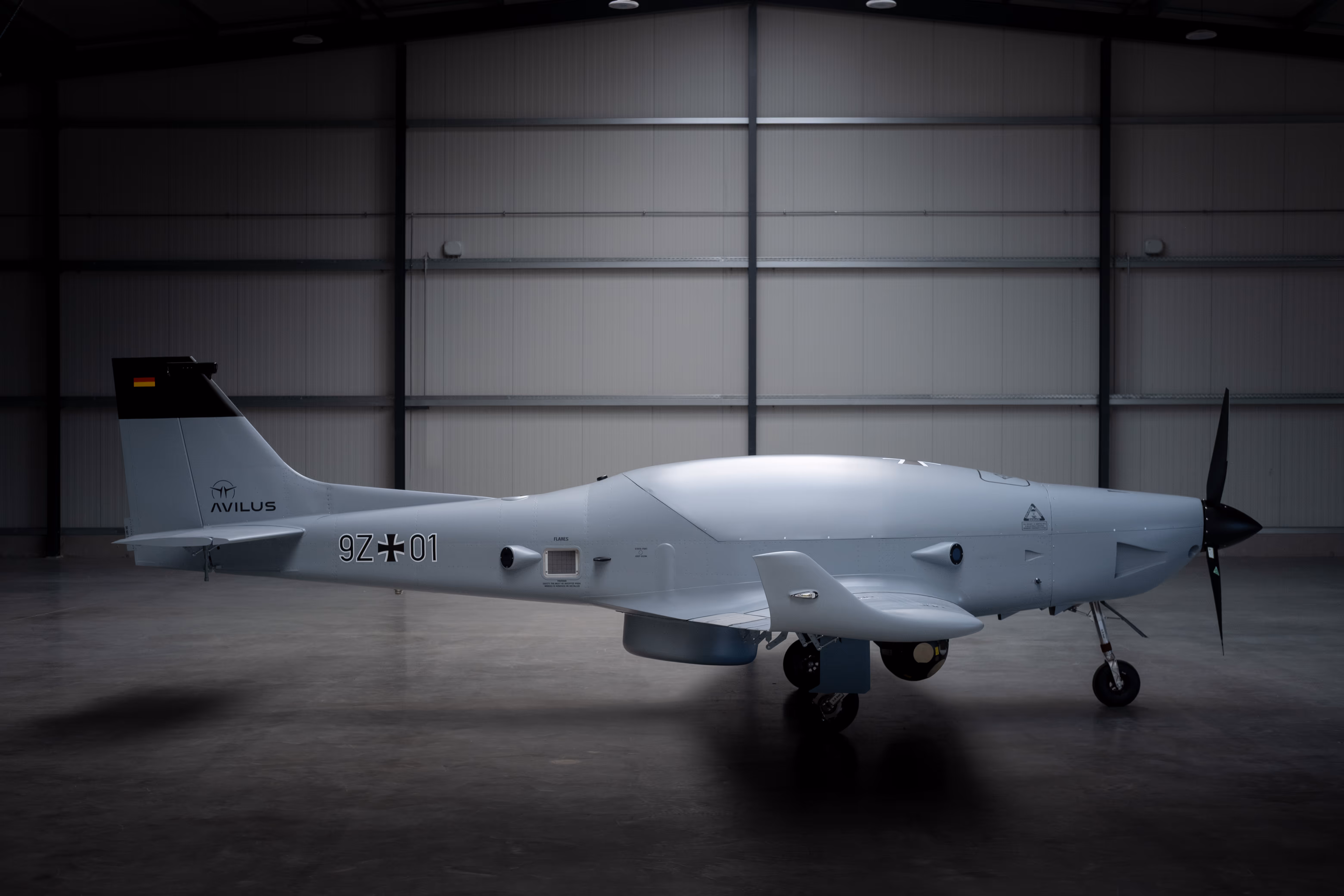 Side view of the Bussard 9Z-01 fixed-wing drone with Avilus tail markings in a hangar.