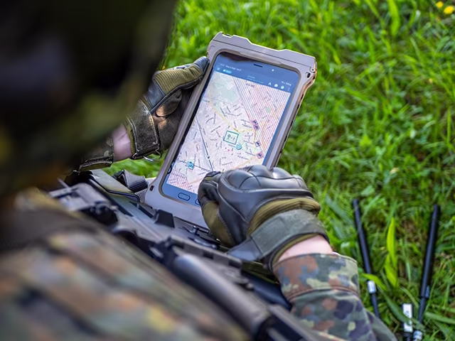 Soldier holding a tablet with a mission map in a field