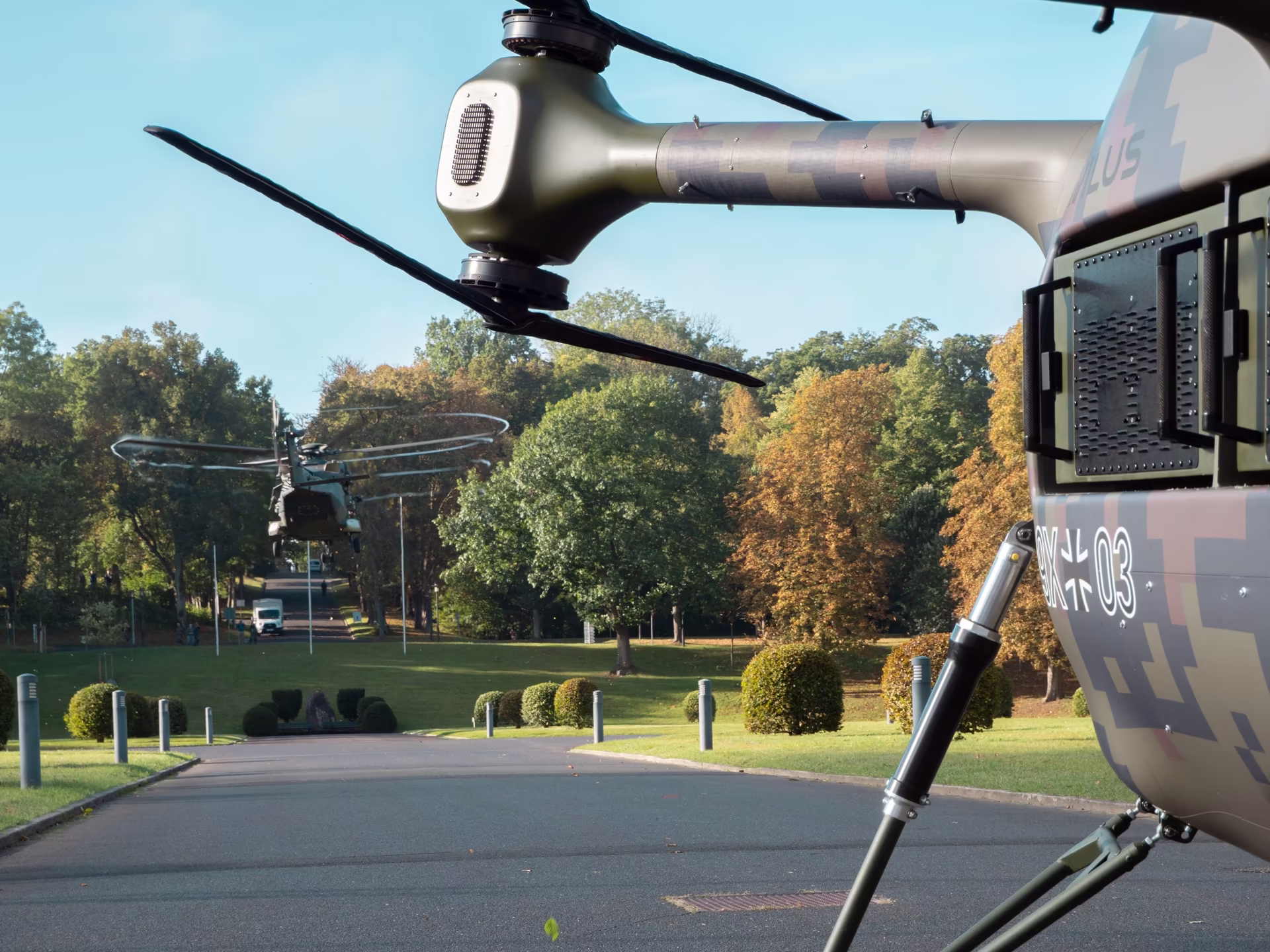 Grille drone hovering in front of an NH90 helicopter in a park