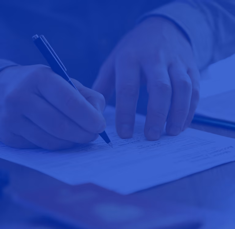 Person writing with a pen on a document placed on a desk.