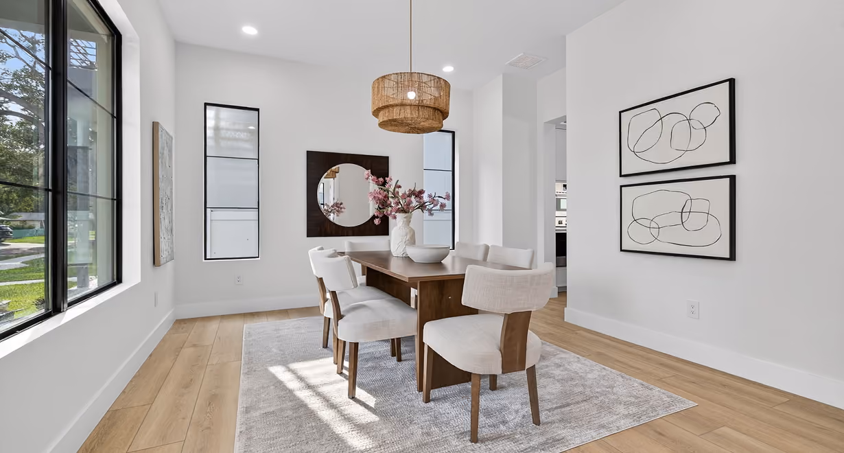 Minimalist dining room with wooden table, six beige chairs, pendant light, wall art, and large windows.