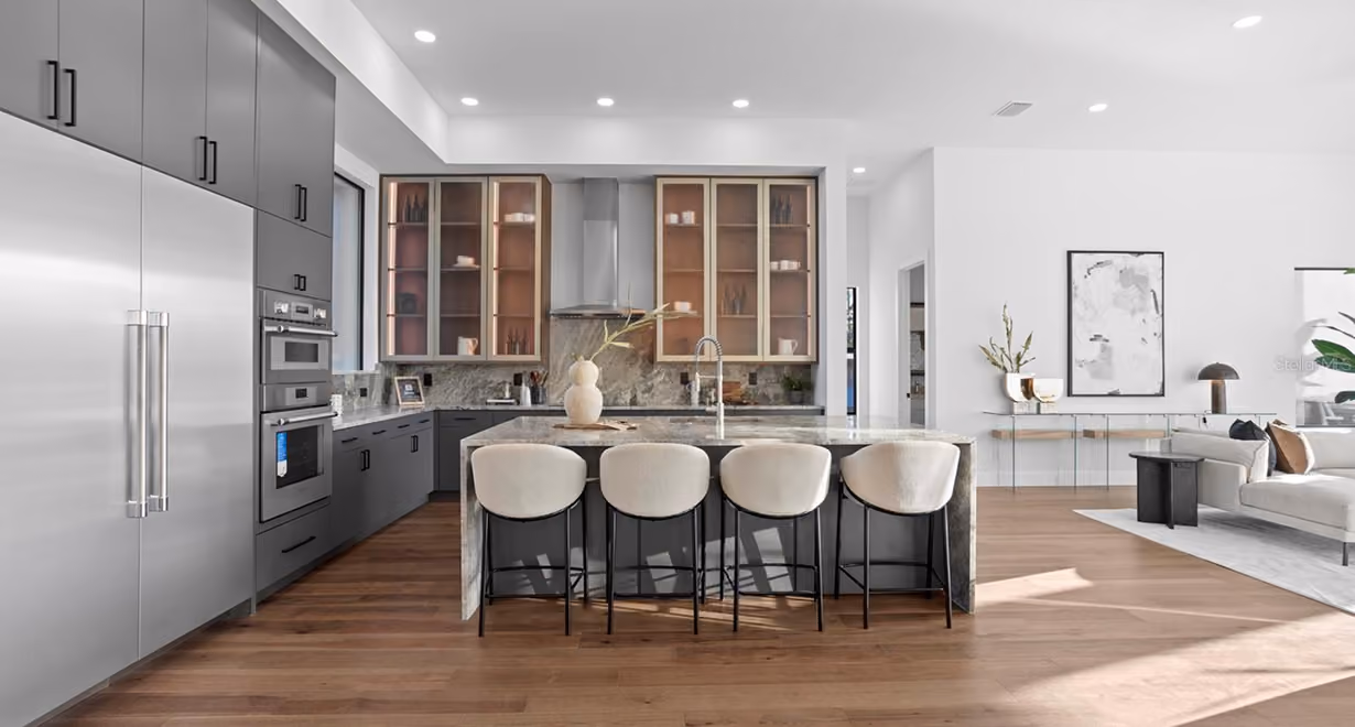 Modern kitchen with gray cabinets, large marble island with four white stools, and hardwood floors.