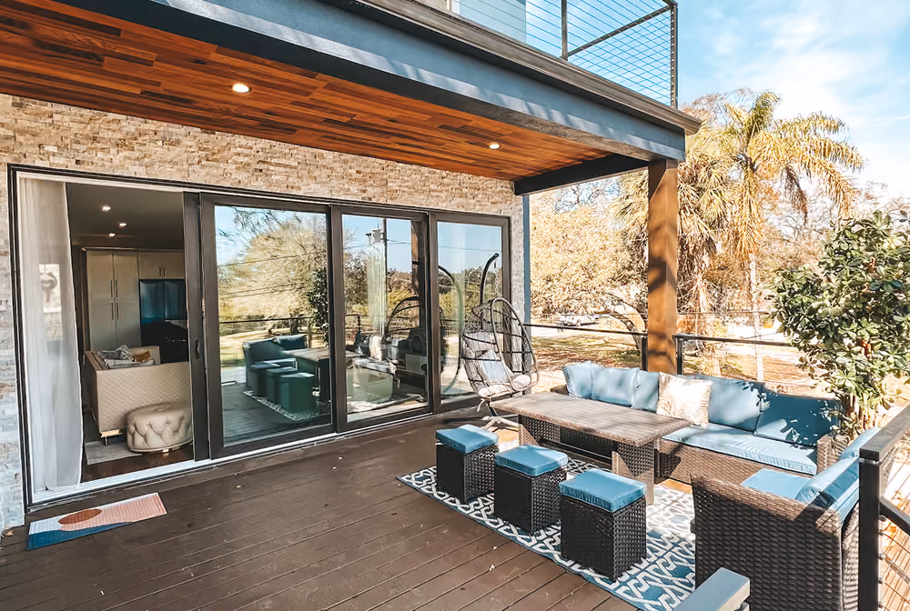Outdoor patio with blue cushioned wicker furniture, hanging chair, and sliding glass doors to indoor living room.