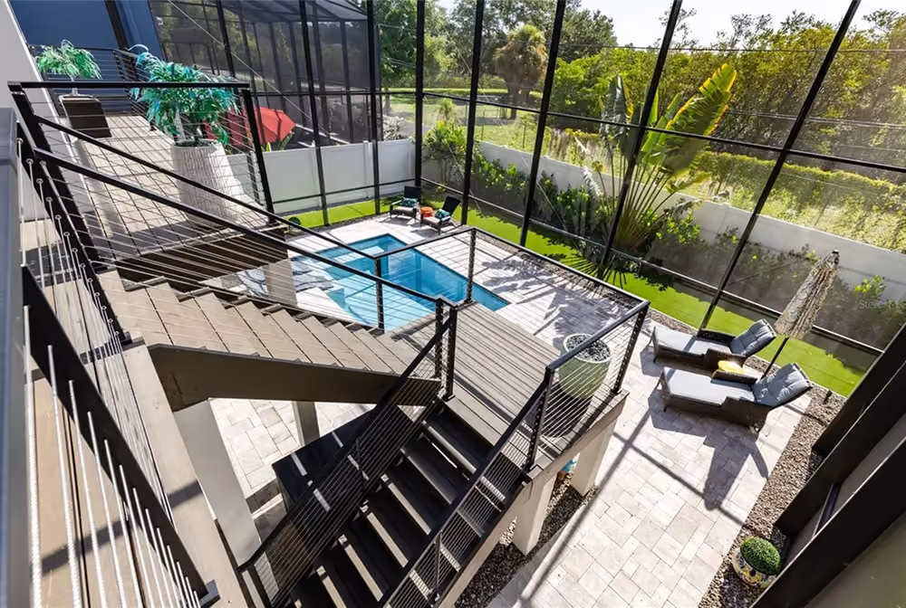 Modern backyard with multi-level deck, small pool, lounge chairs, plants, and glass railing.