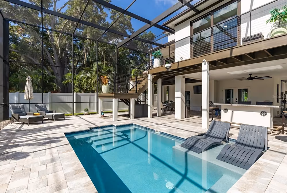 Backyard pool with two lounge chairs submerged on shallow platform and shaded patio area.