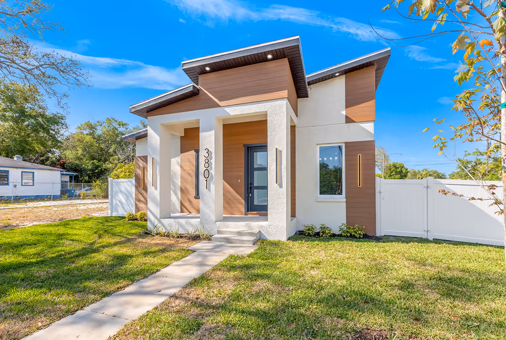 Modern single-story house with white walls, wood accents, and a front lawn under a blue sky.