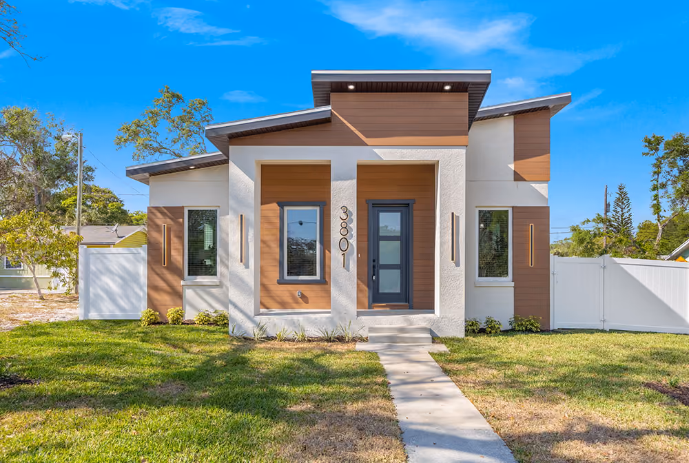 Modern single-story home with white and wood panel exterior, black door, and grassy front yard.