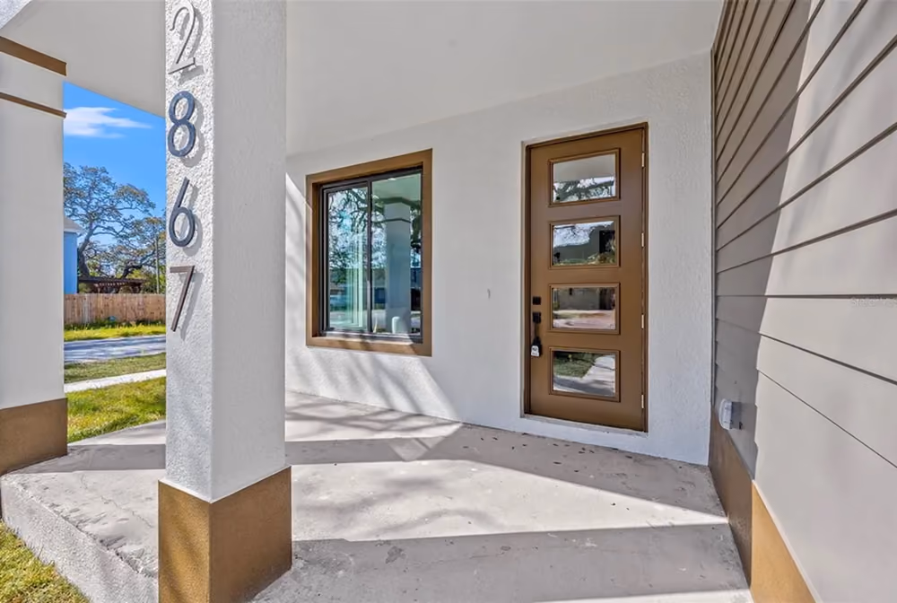 House entrance with a brown door and window, white walls, and address numbers 2867 on a pillar.