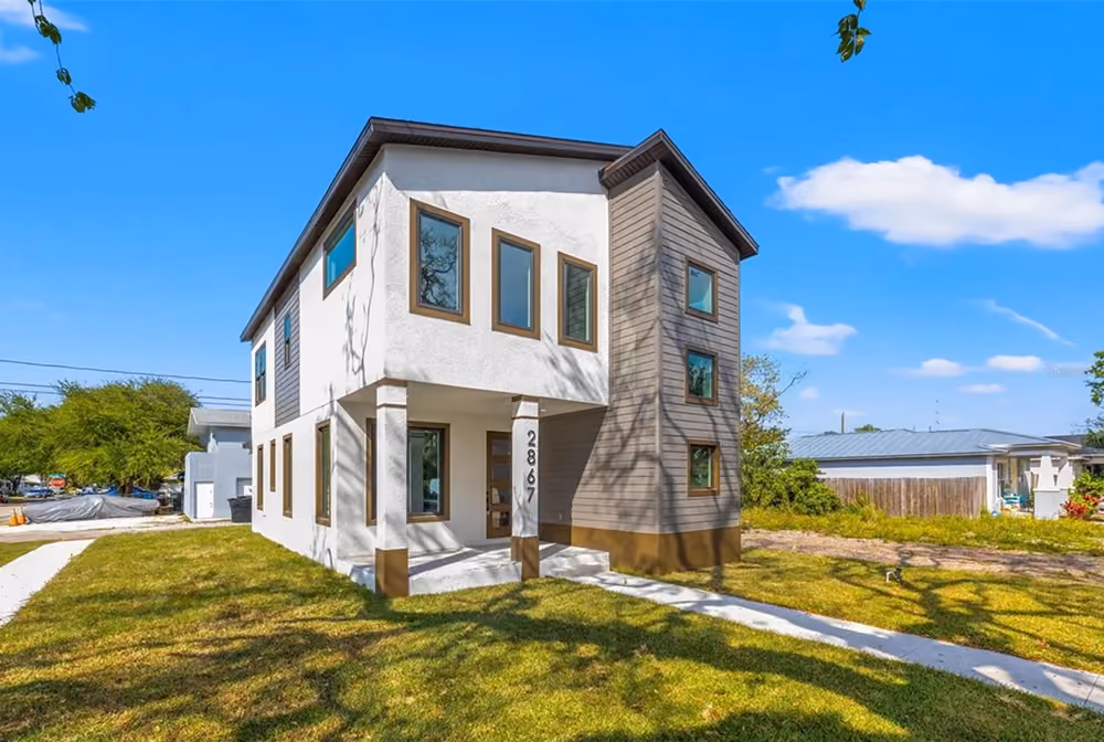 Modern two-story house with white and gray exterior surrounded by grass under a blue sky.