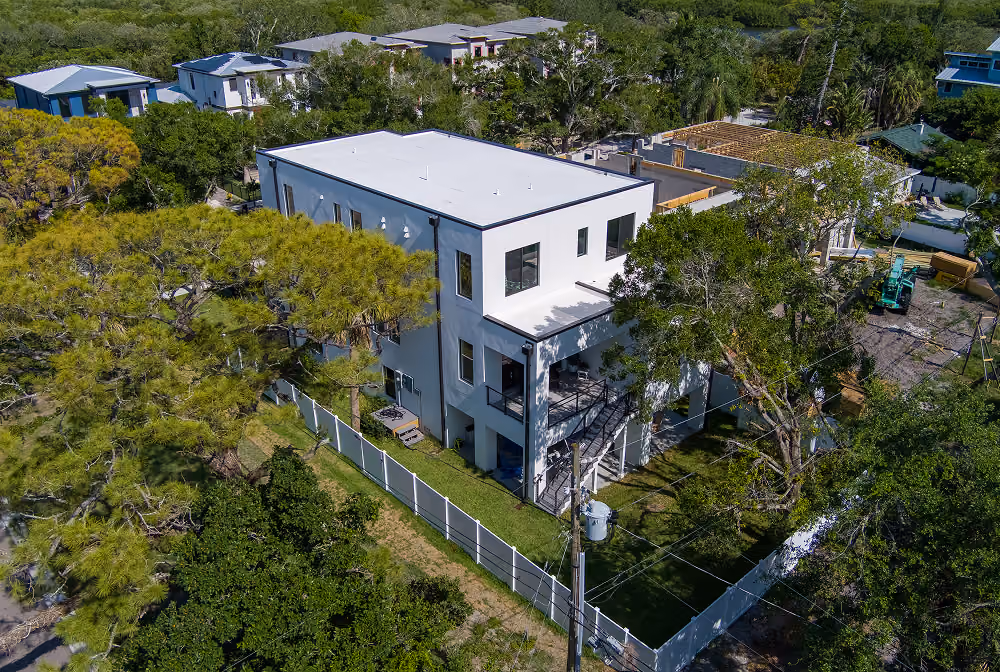 Aerial view of a modern white two-story house surrounded by trees and a white fence.