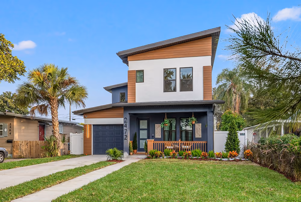 Modern two-story house with a front porch, garage, palm trees, and green lawn on a clear day.