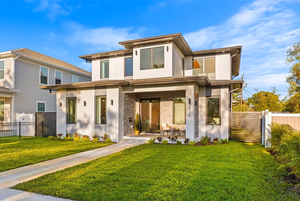 Modern two-story house with white exterior, large windows, and a well-kept green lawn in front.