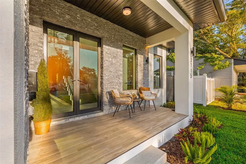 Modern porch with two wicker chairs, a small table, potted plant, and glass double doors.