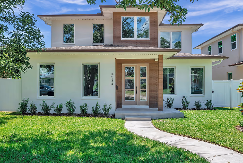 Modern two-story house with white exterior, large windows, and a curved concrete front walkway on green lawn.